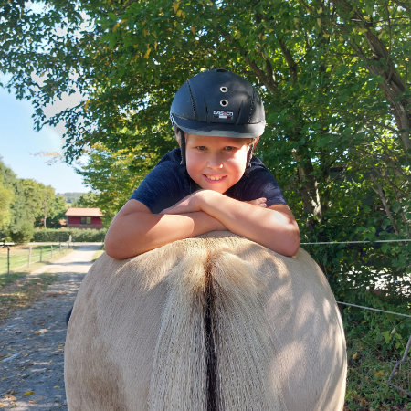 Reiten Therapie Söhrewald Ein Junge liegt auf einem Pferderücken und schaut in die Kamera.